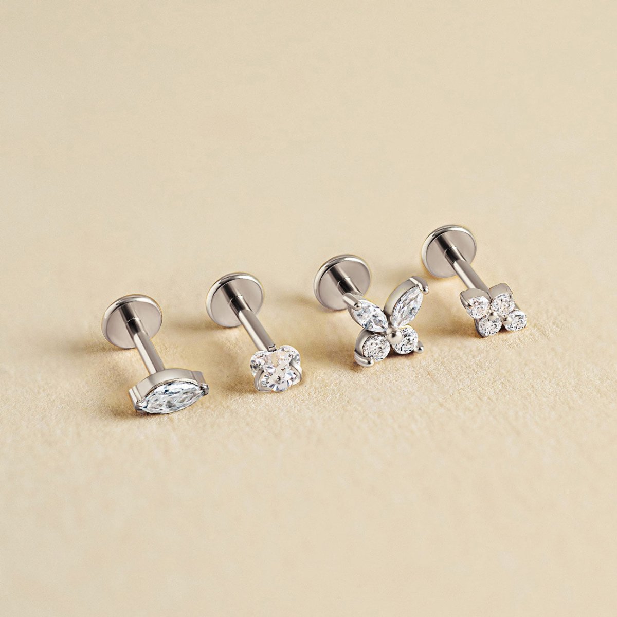 Four silver flat back studs with clear stones in marquise, round and cluster shapes, on a cream background | #Gemstone_White Zirconia