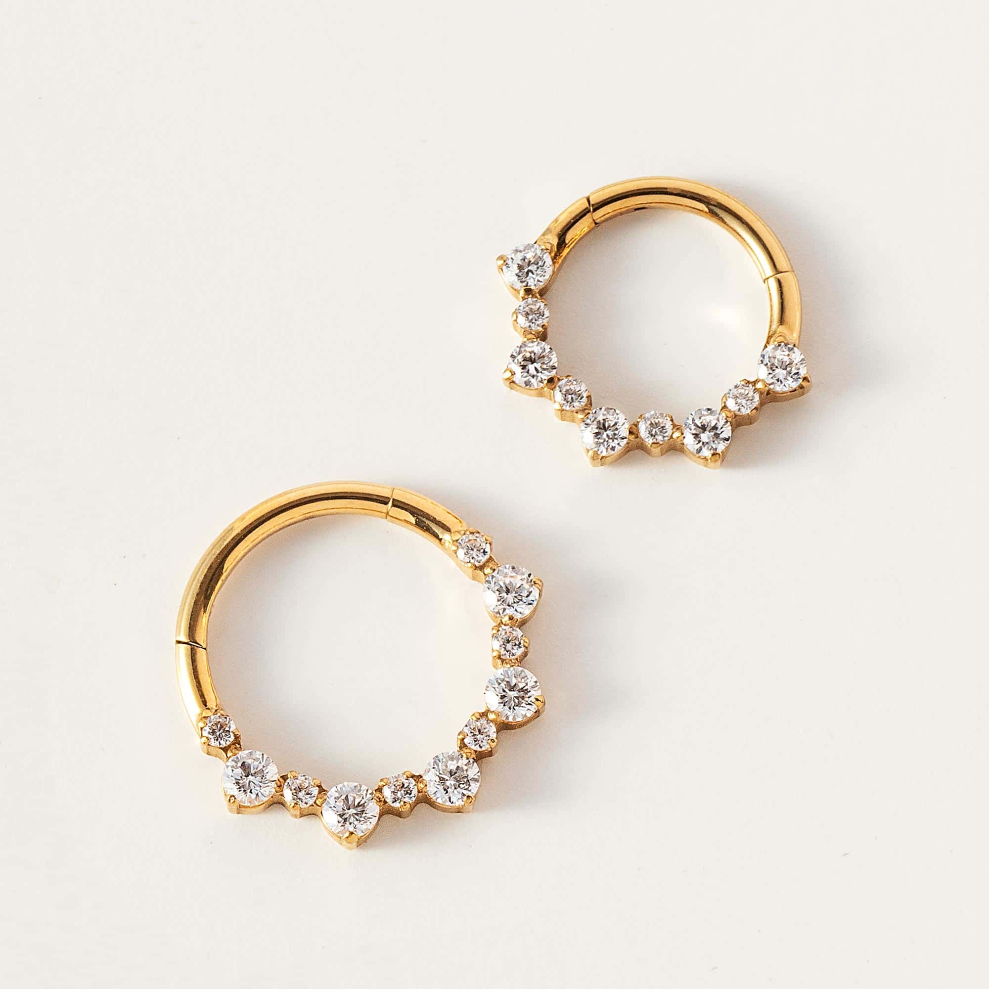 Two gold titanium seamless clicker hoops with round clear stones, on a cream background