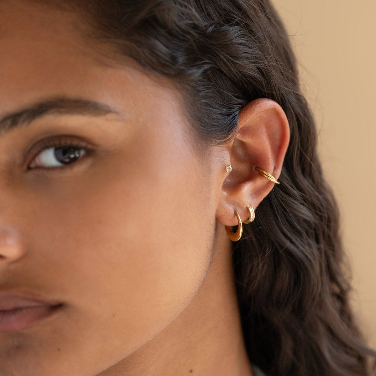 Gold hoops, a pavé huggie, an ear cuff and a clear stud styled in an ear stack on a model