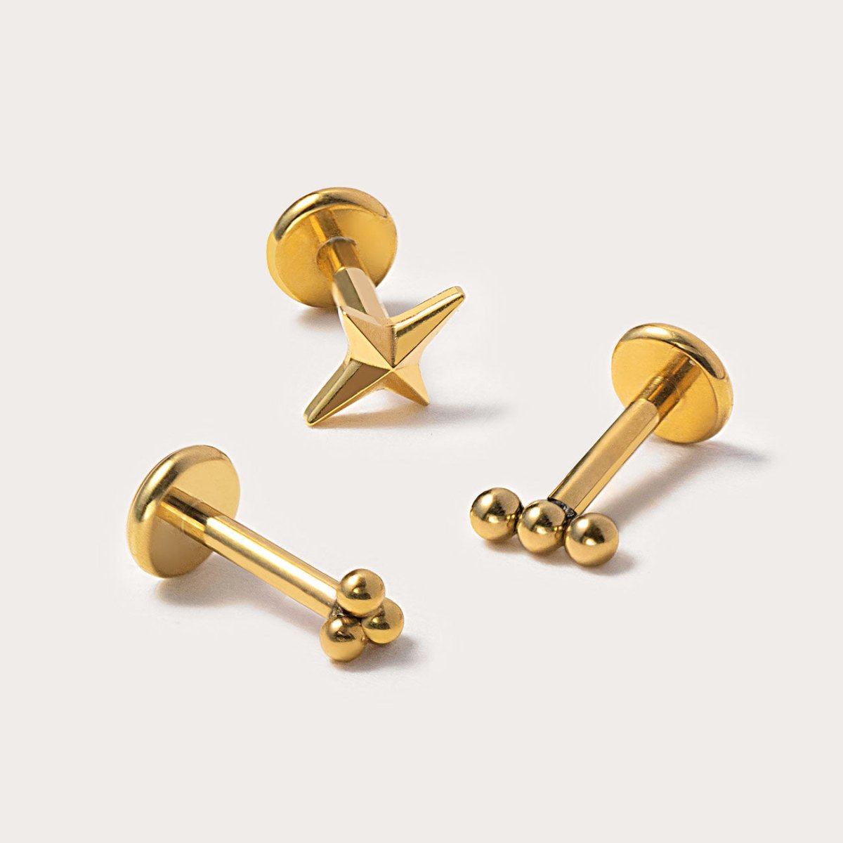 Gold titanium flat back studs, a star and two trinity ball styles, on a light background