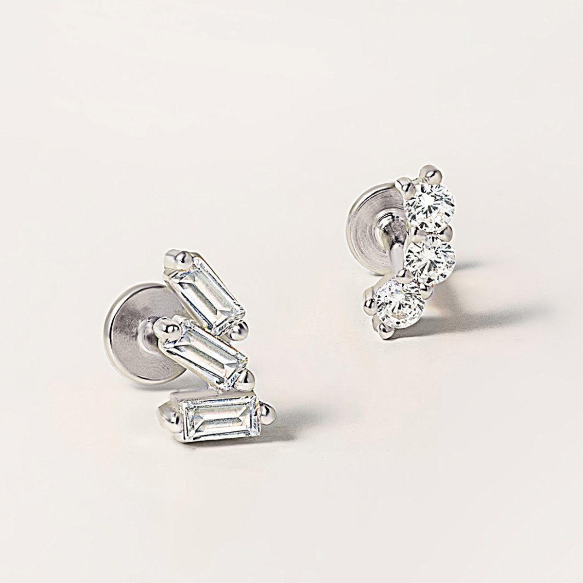 Silver flat back studs with baguette and round clear stones, close-up on a cream background