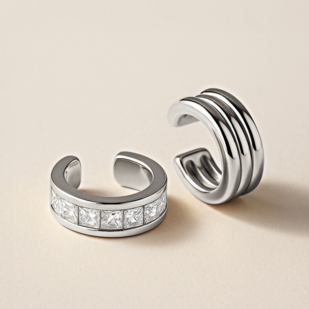Silver ridged ear cuff beside a square clear-stone band ear cuff, on a cream background