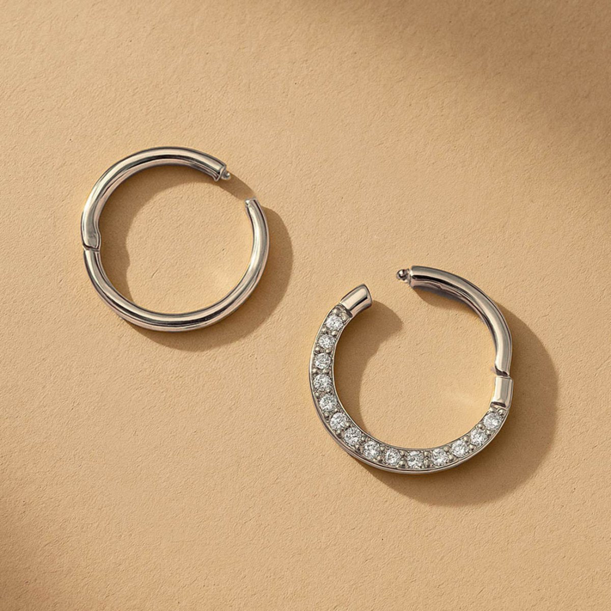Two silver seamless clicker hoops, one plain and one pavé with clear stones, on a cream background