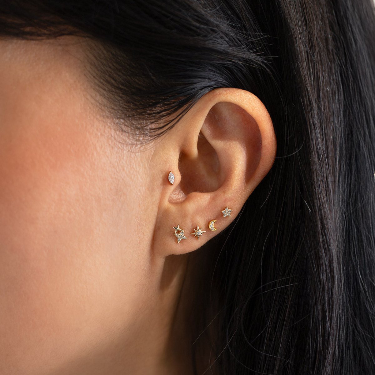 Gold star, marquise and moon studs with clear stones shown stacked on a model's ear