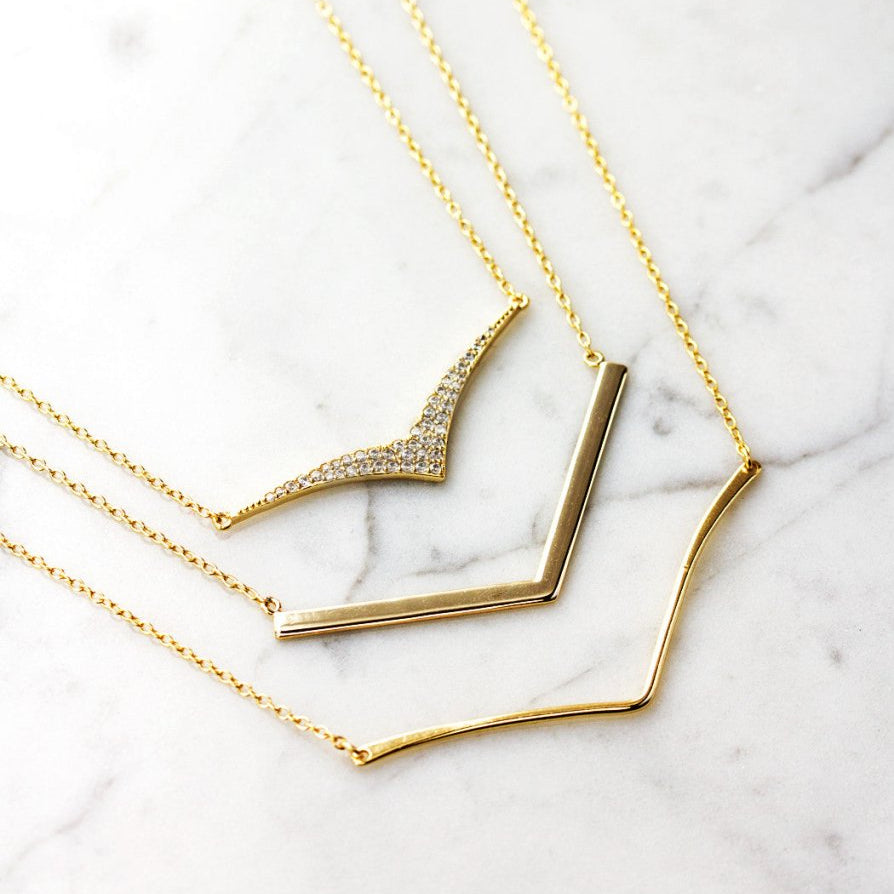 Gold vermeil pave chevron necklace shown layered with plain chevron necklaces, on white marble