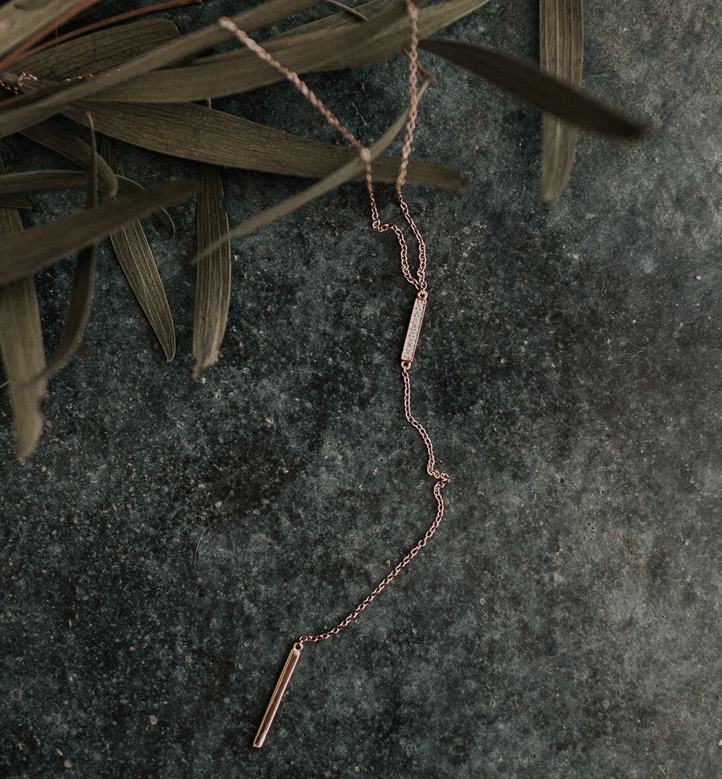 Rose gold vermeil pavé bar lariat necklace laid on gray slate with dried leaves