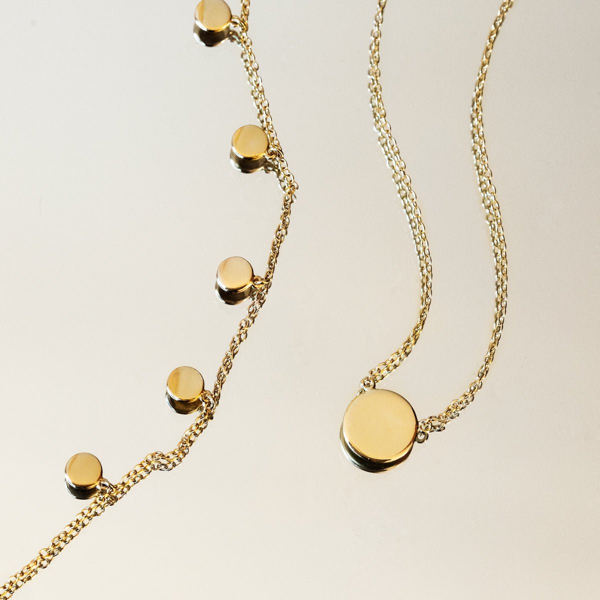 Gold vermeil disc dangle bracelet shown beside a matching disc pendant necklace, on a cream background