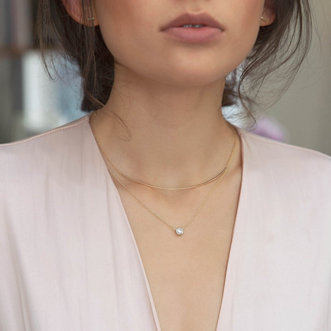 Gold vermeil curved bar necklace shown on a model's neckline, layered with a stone pendant