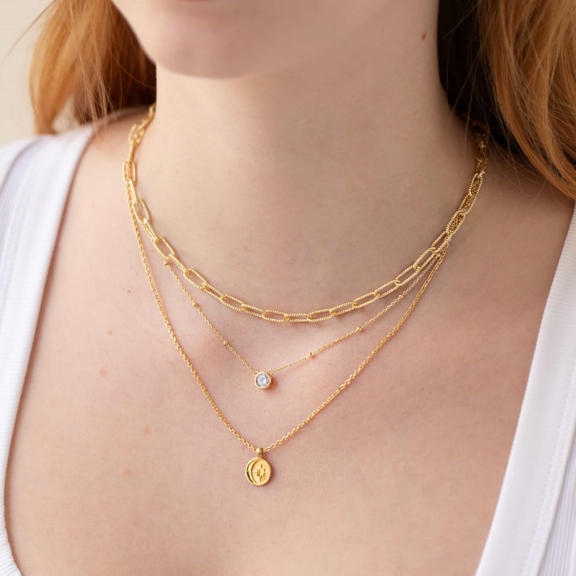Layered gold chains with a moon-and-star coin pendant, shown on a model's neckline
