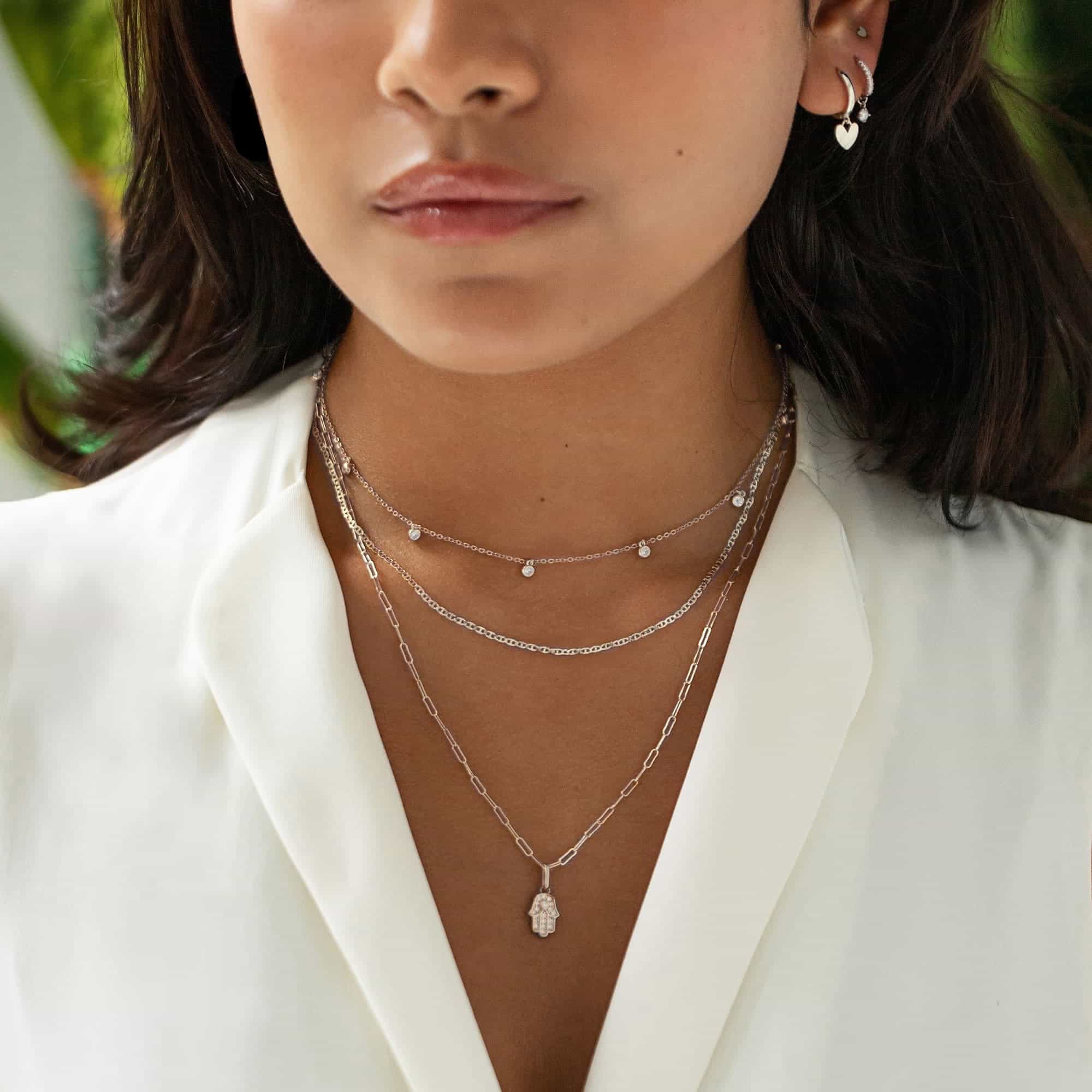 Layered silver chains with a pavé hamsa charm and station drops on a model's neckline