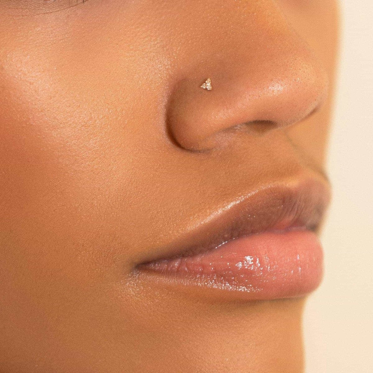 14K gold clover nose stud with clear stones, shown on a model's nose