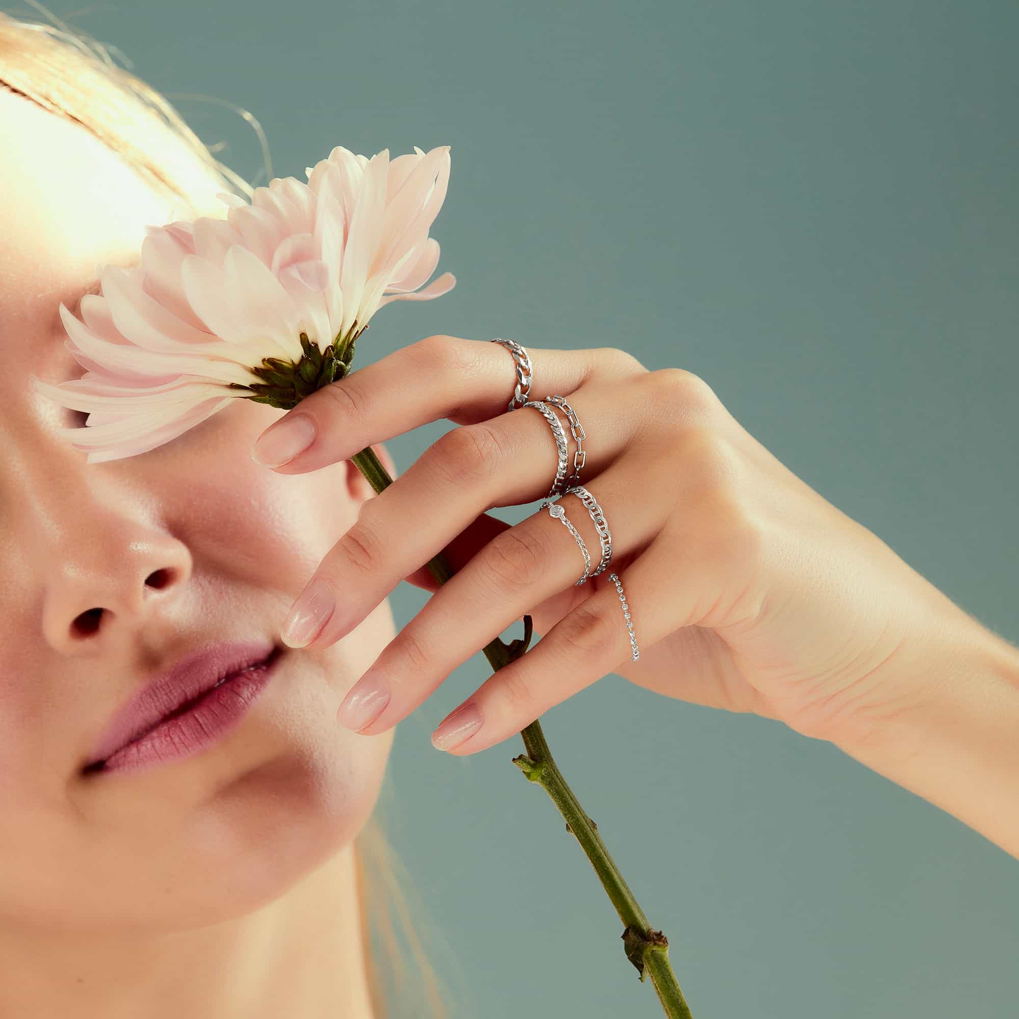 Sterling silver chain rings worn in a stack on a model's hand holding a flower