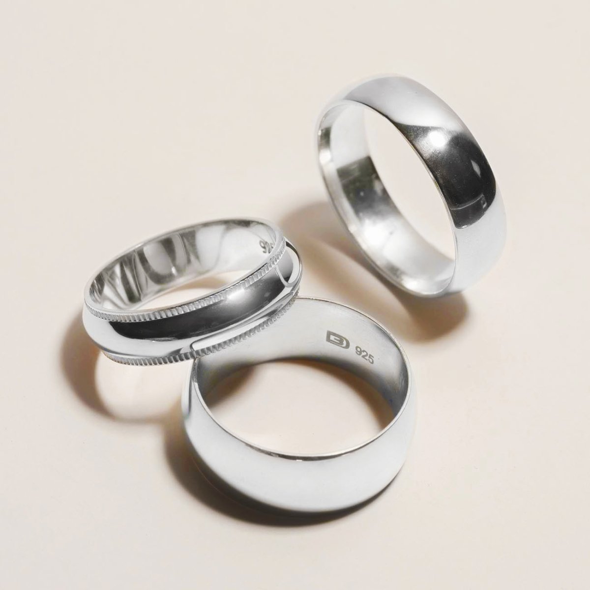 Three sterling silver band rings including a milgrain edge band, on a cream background