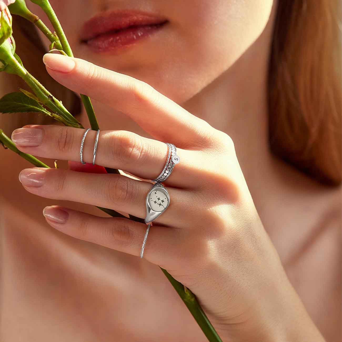 Sterling silver thin stacking rings shown on a model's hand holding a rose