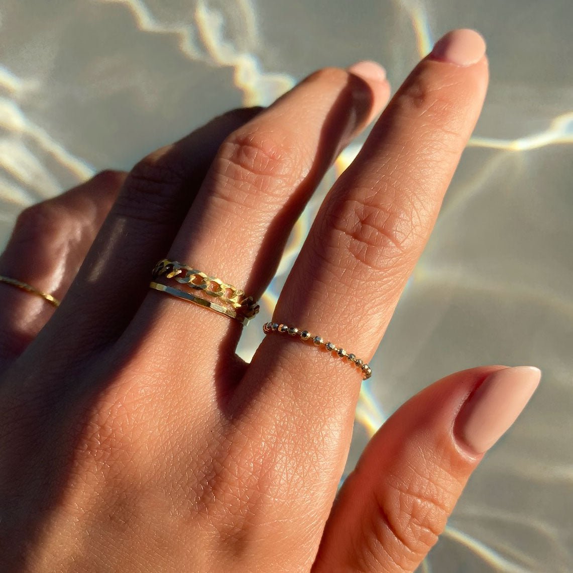 Gold-filled hammered thin stacking rings shown on a model's fingers in sunlight