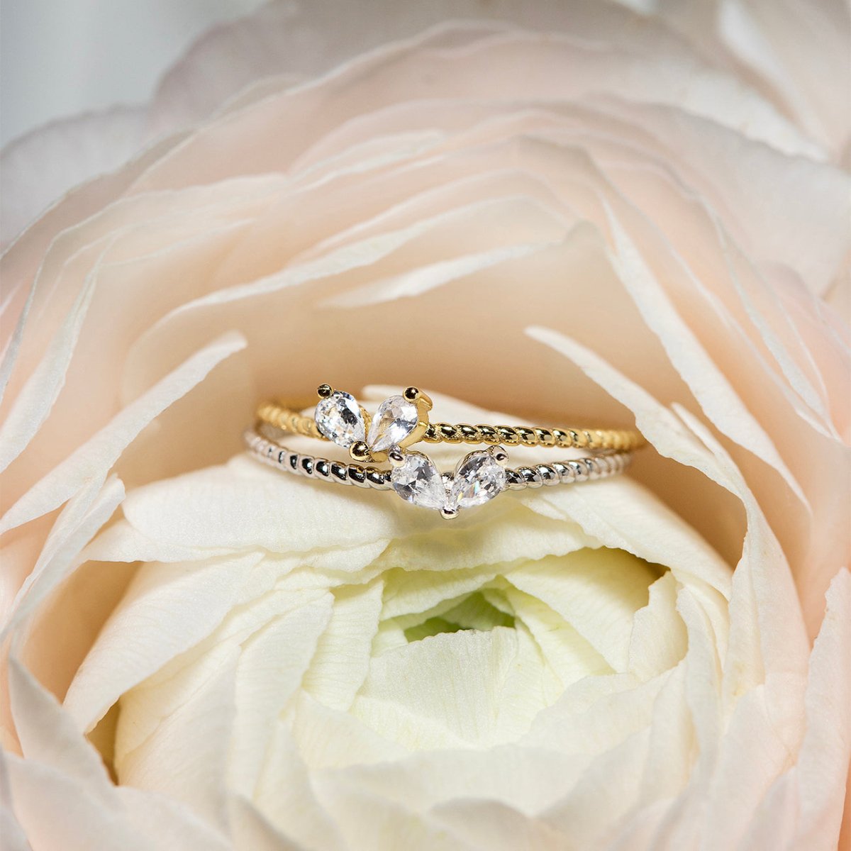 Gold vermeil and silver twin pear white zirconia rings resting on a pale pink rose petal