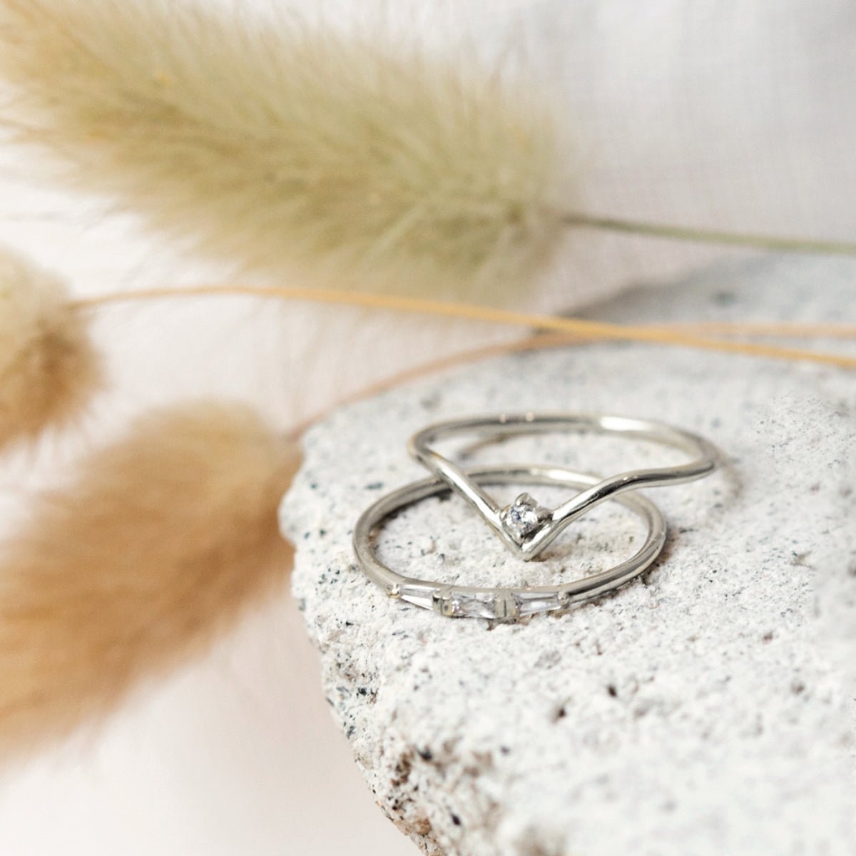 Sterling silver baguette ring with clear stones, beside a chevron ring on a stone surface
