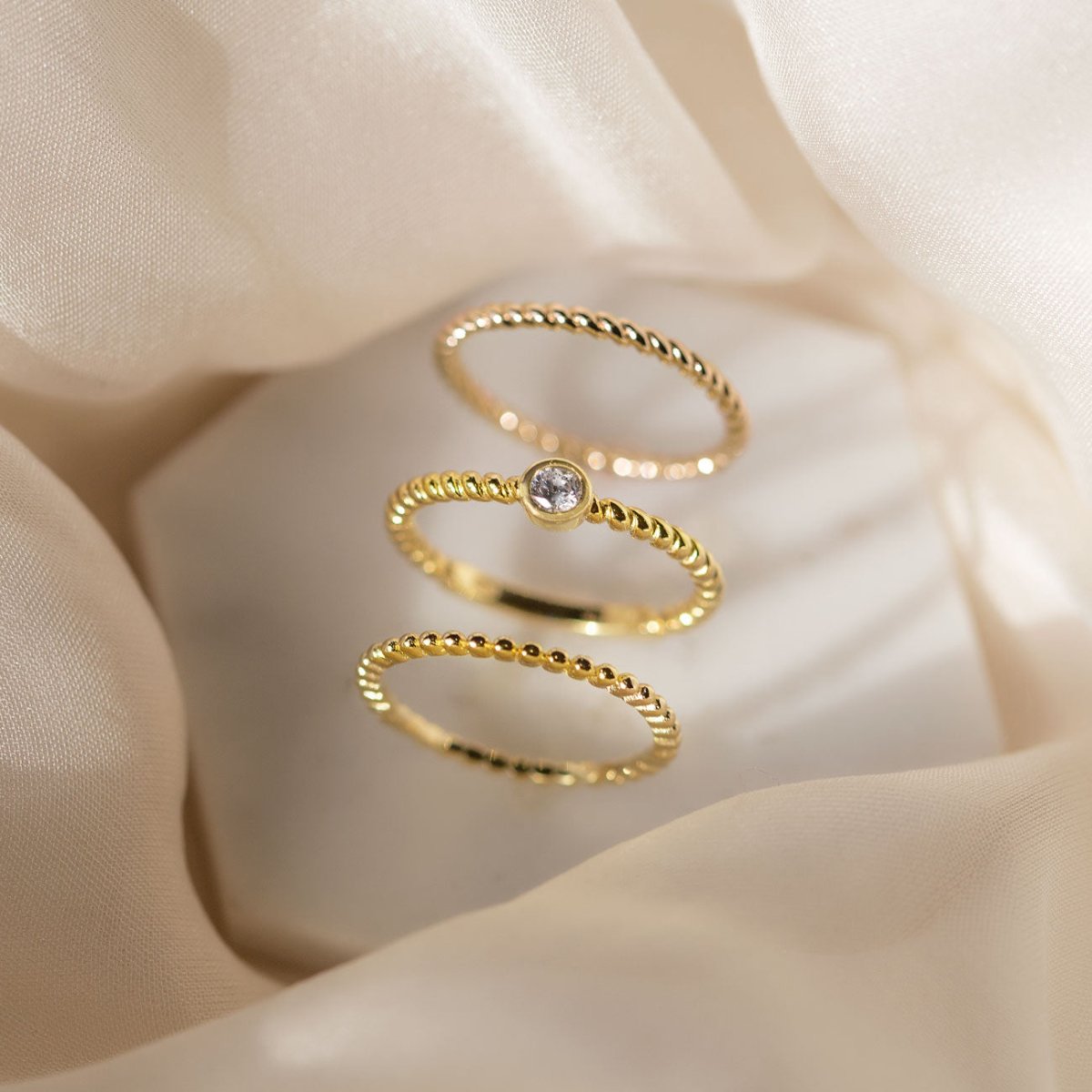 Gold vermeil solitaire rope ring with a clear stone, shown in a stack of beaded bands on a cream background