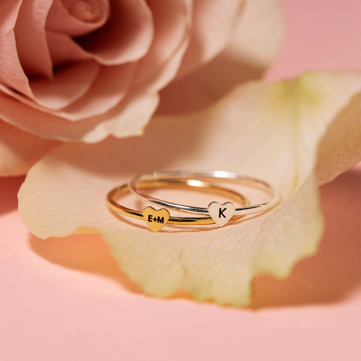 Sterling silver and gold tiny heart initial rings engraved with initials, resting on a rose petal