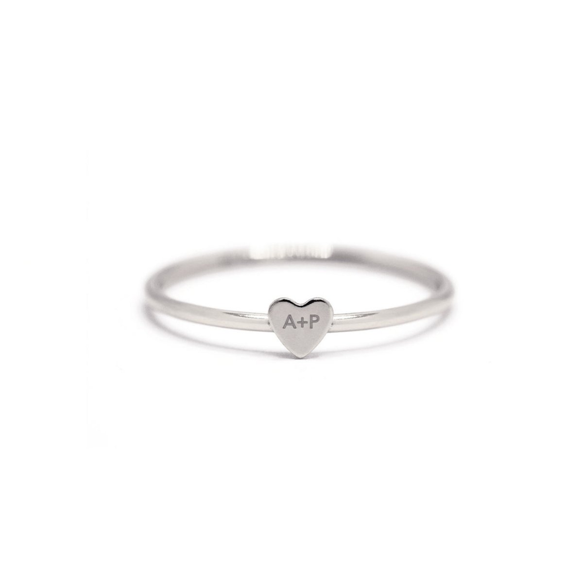 Sterling silver thin band ring with a tiny heart engraved with initials, on a white background