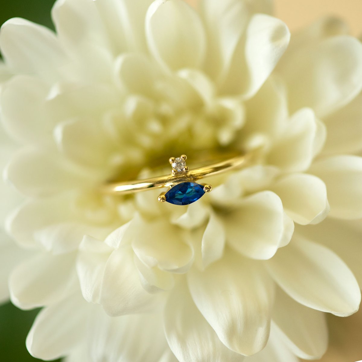 Gold vermeil blue sapphire marquise ring with a small clear accent stone, resting on a white flower