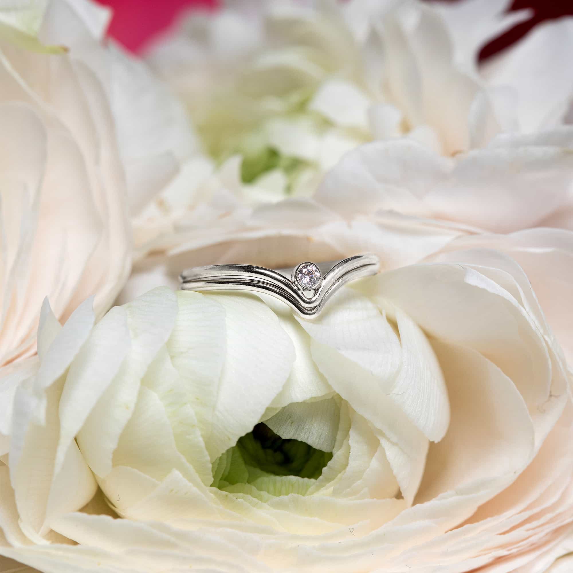 Sterling silver chevron ring with a clear stone at the point, nestled in white petals