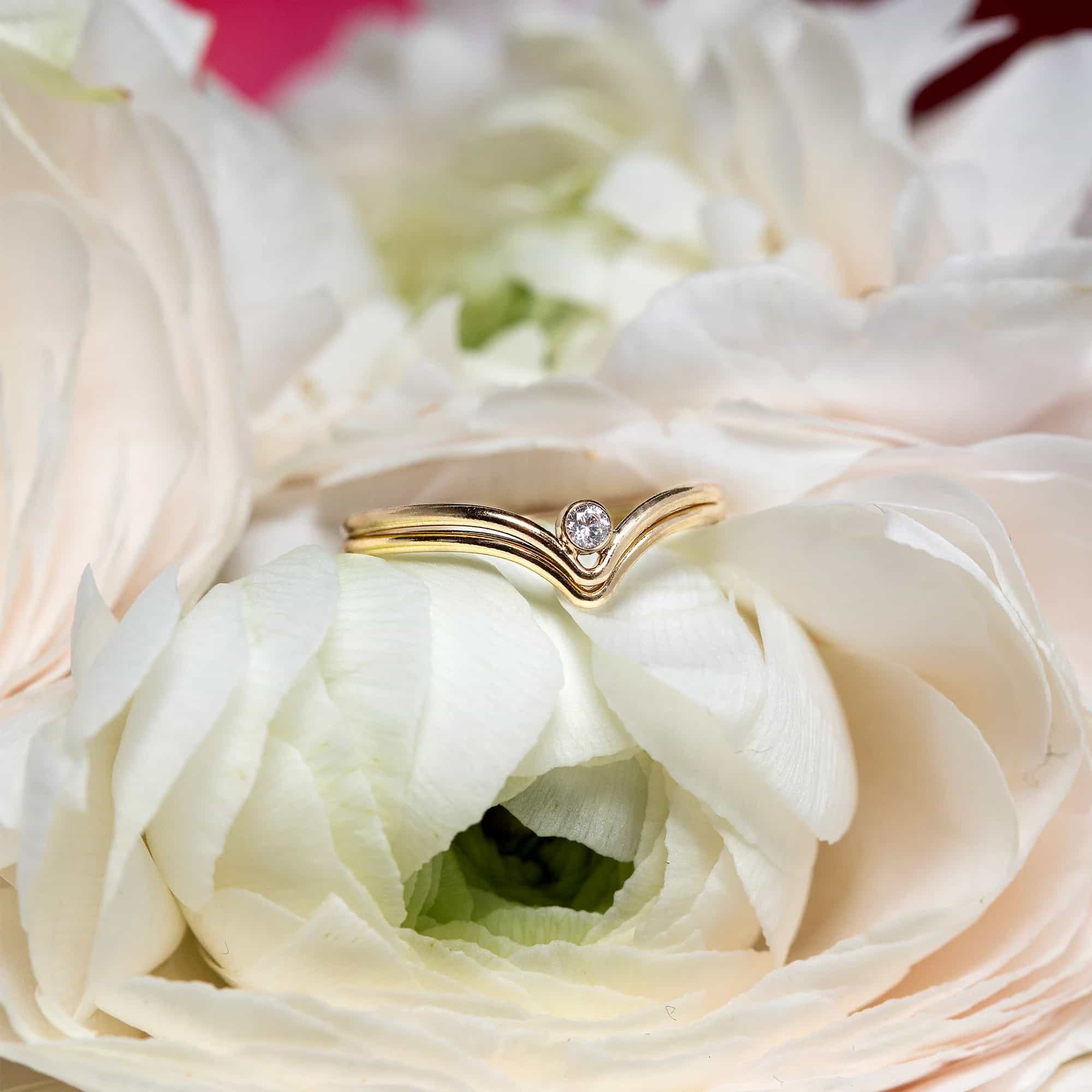 Gold chevron ring with a small clear stone, resting on white ranunculus petals