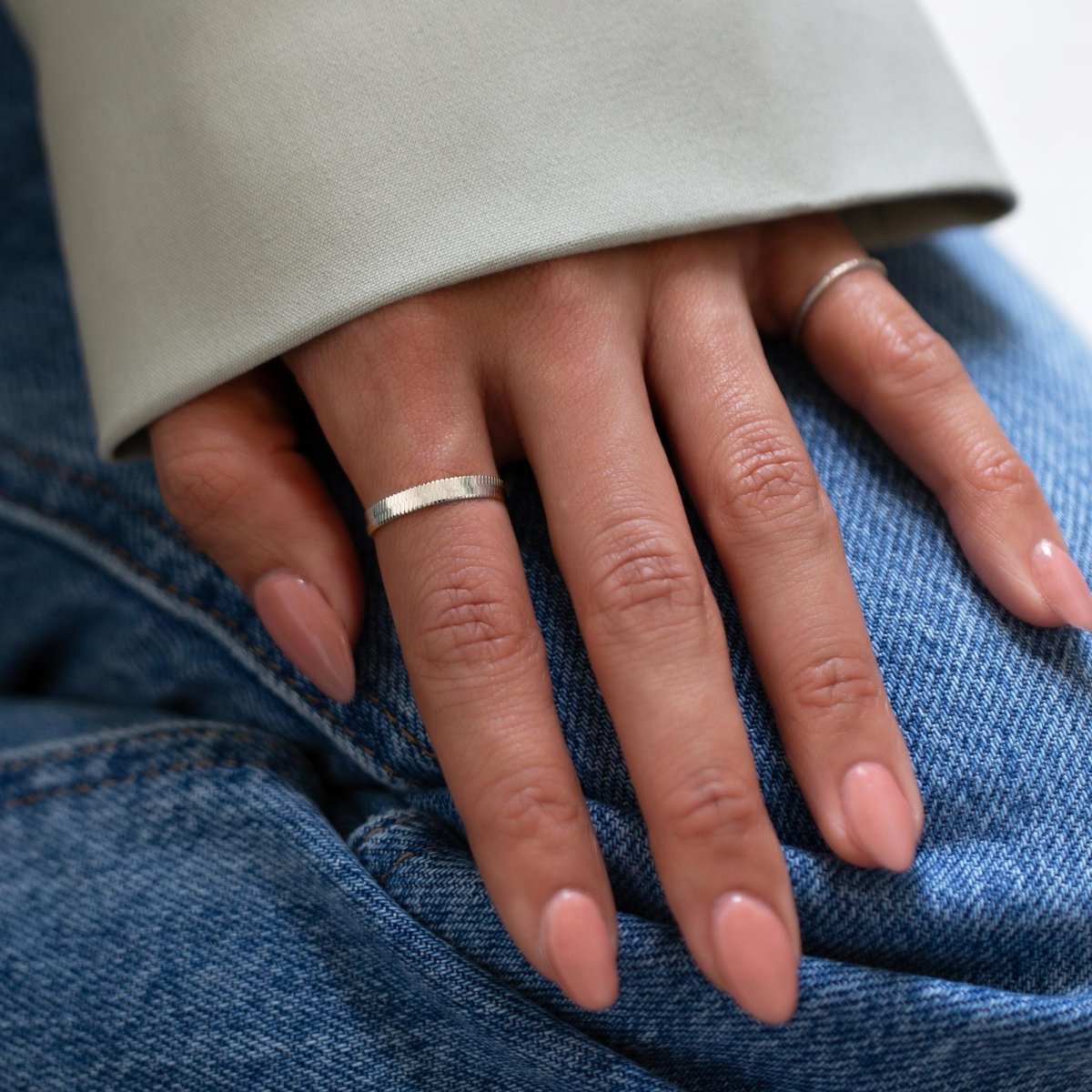Sterling silver herringbone chain stacking ring shown on a model's finger resting on denim