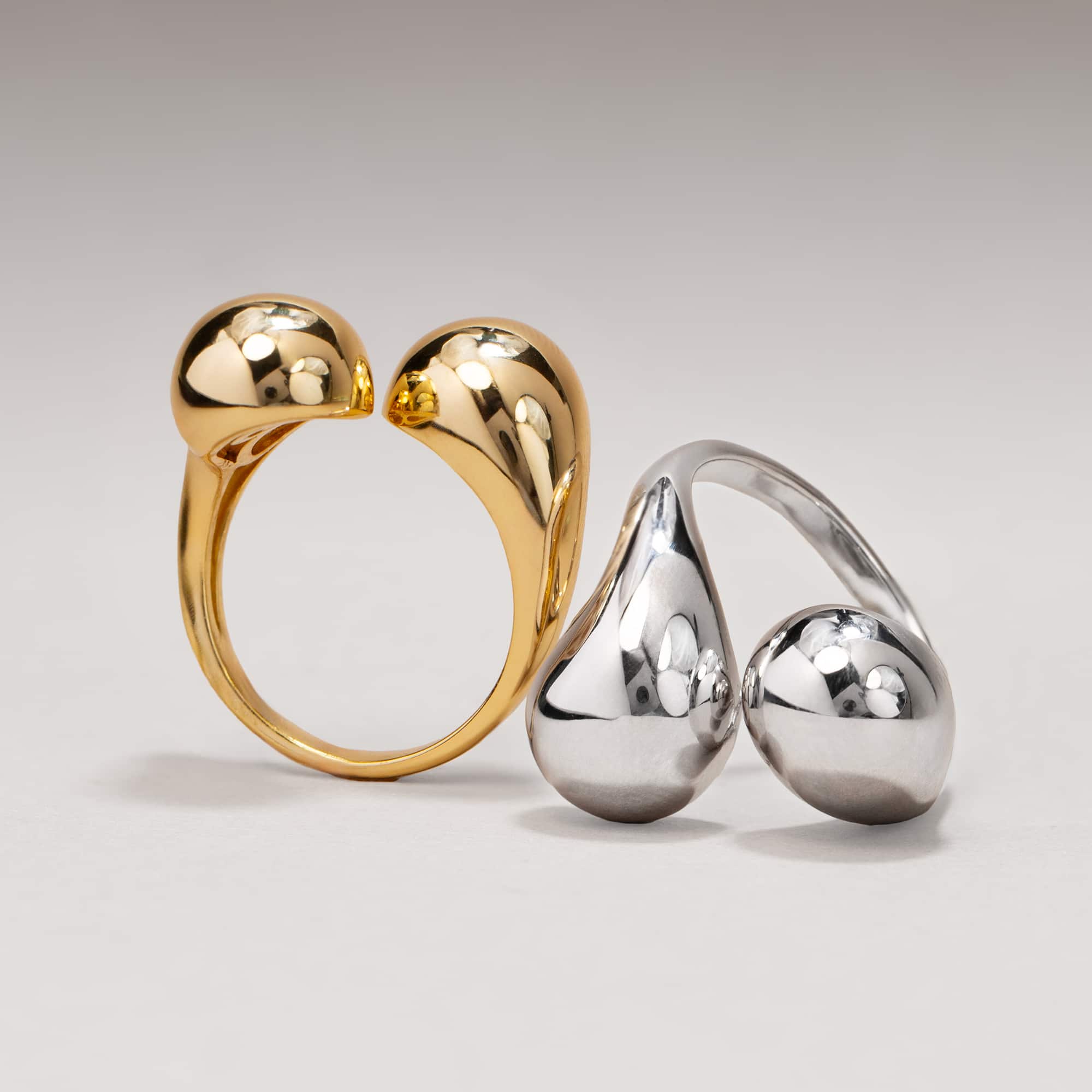 Gold vermeil and sterling silver sculptural bypass rings shown together, on a cream background