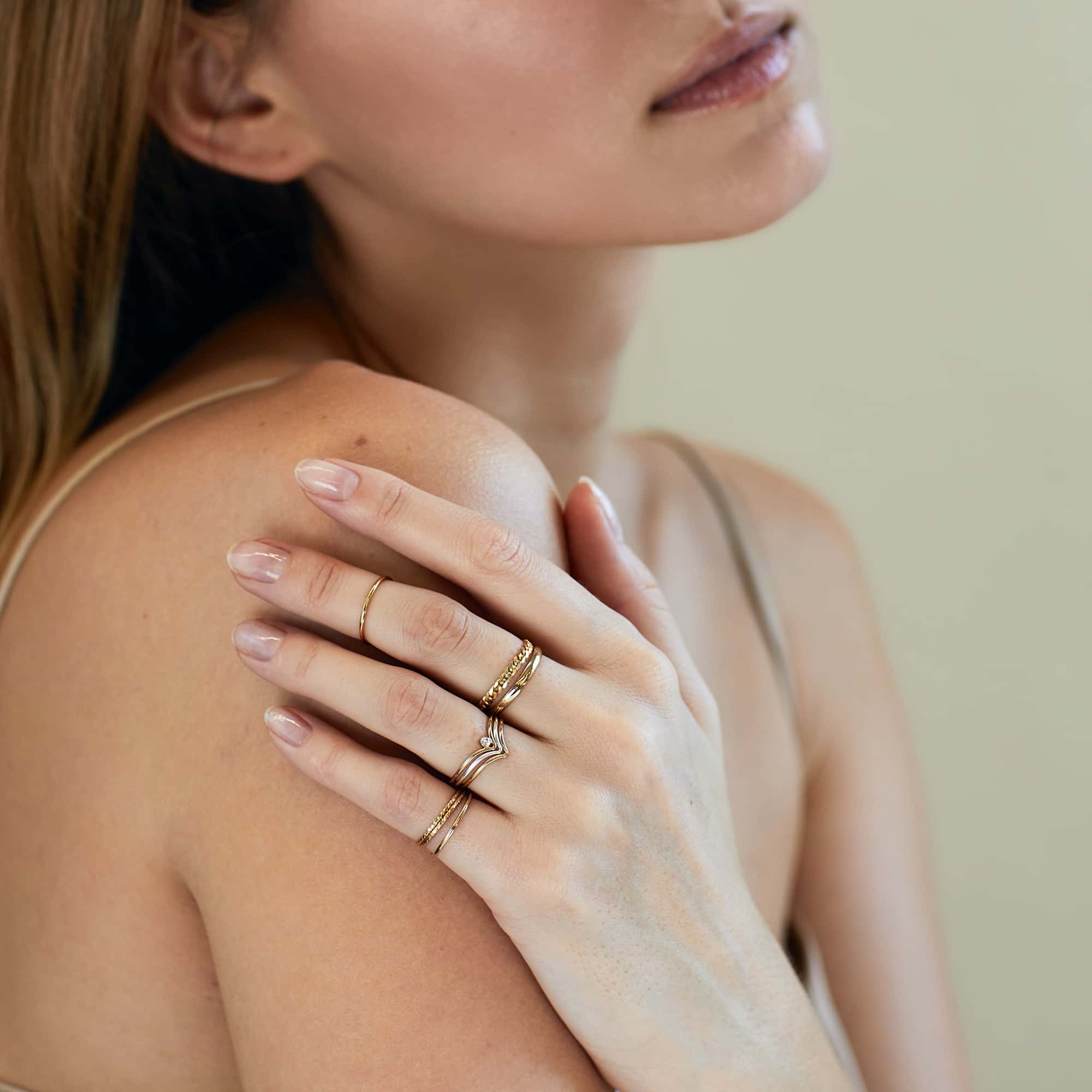 14K gold chevron ring stacked with other rings, shown on a model's hand at the shoulder