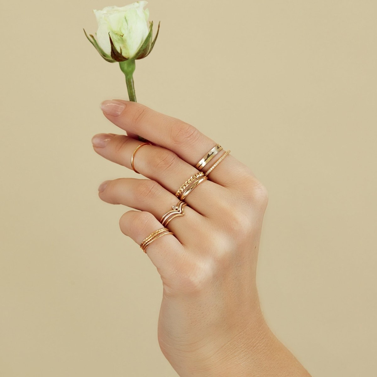 14K gold thin band rings stacked on a model's fingers, holding a white rosebud