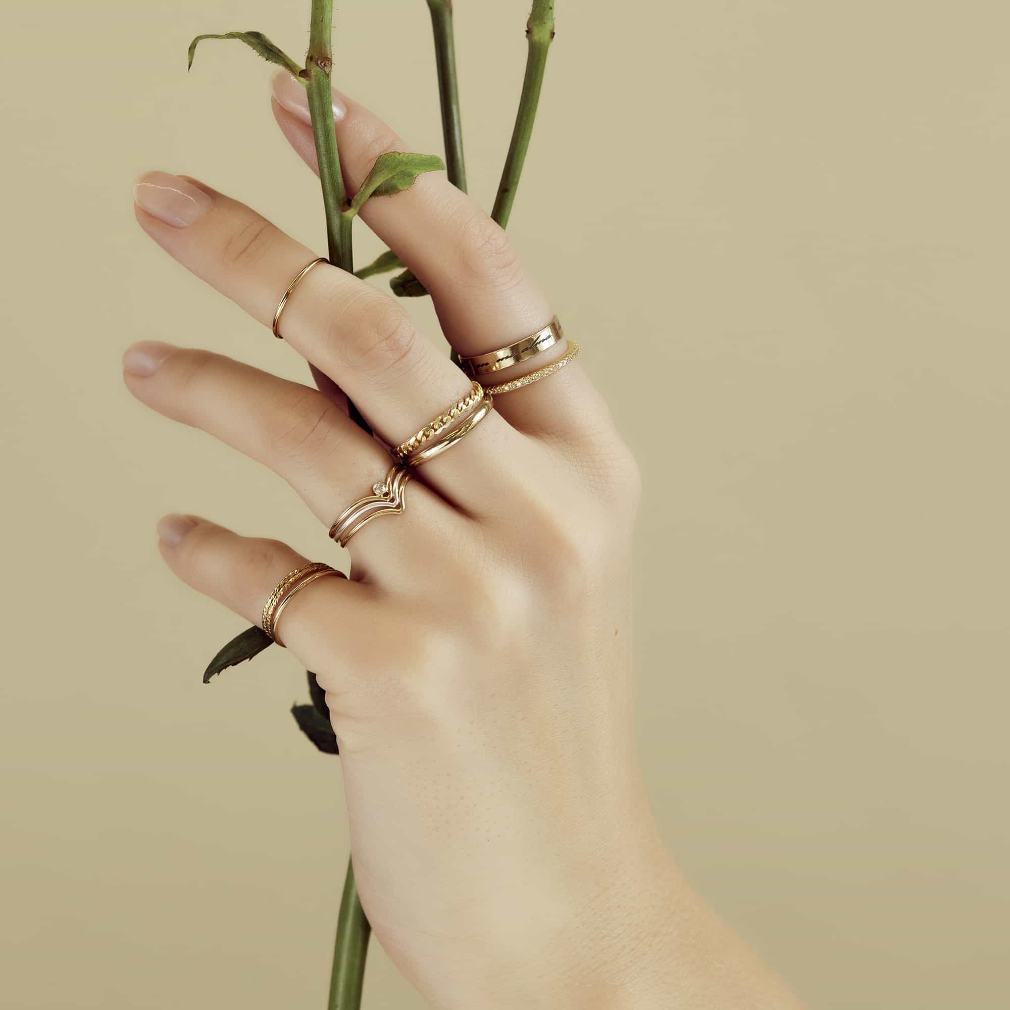 Assortment of gold stacking and pavé rings layered on a model's hand holding a rose stem