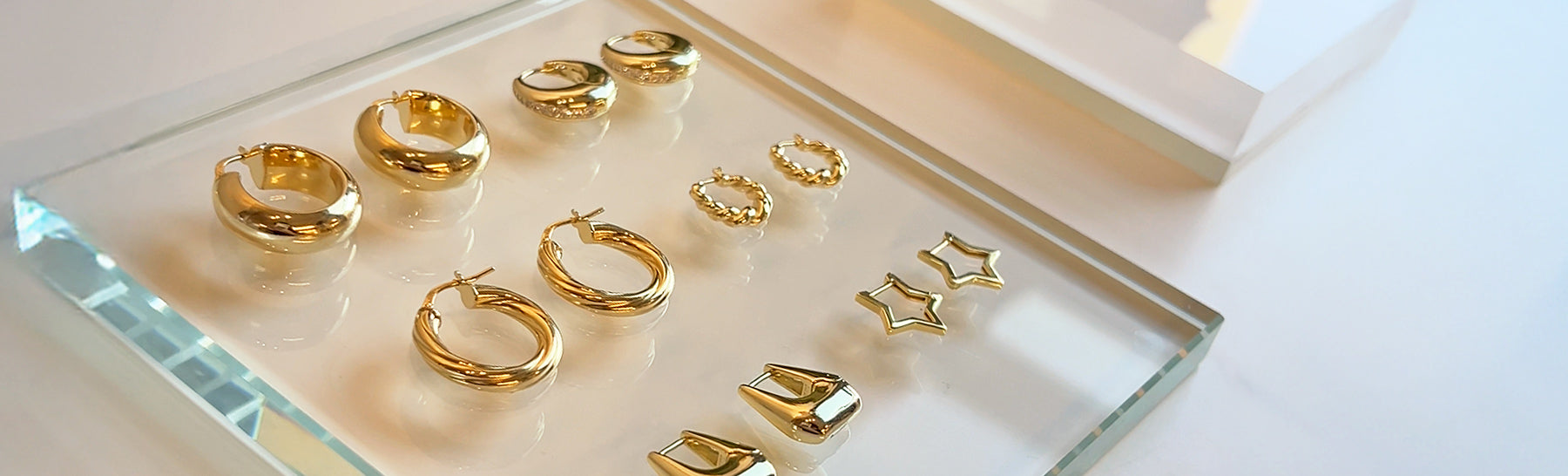 Assorted gold hoop and stud earrings displayed on a glass tray