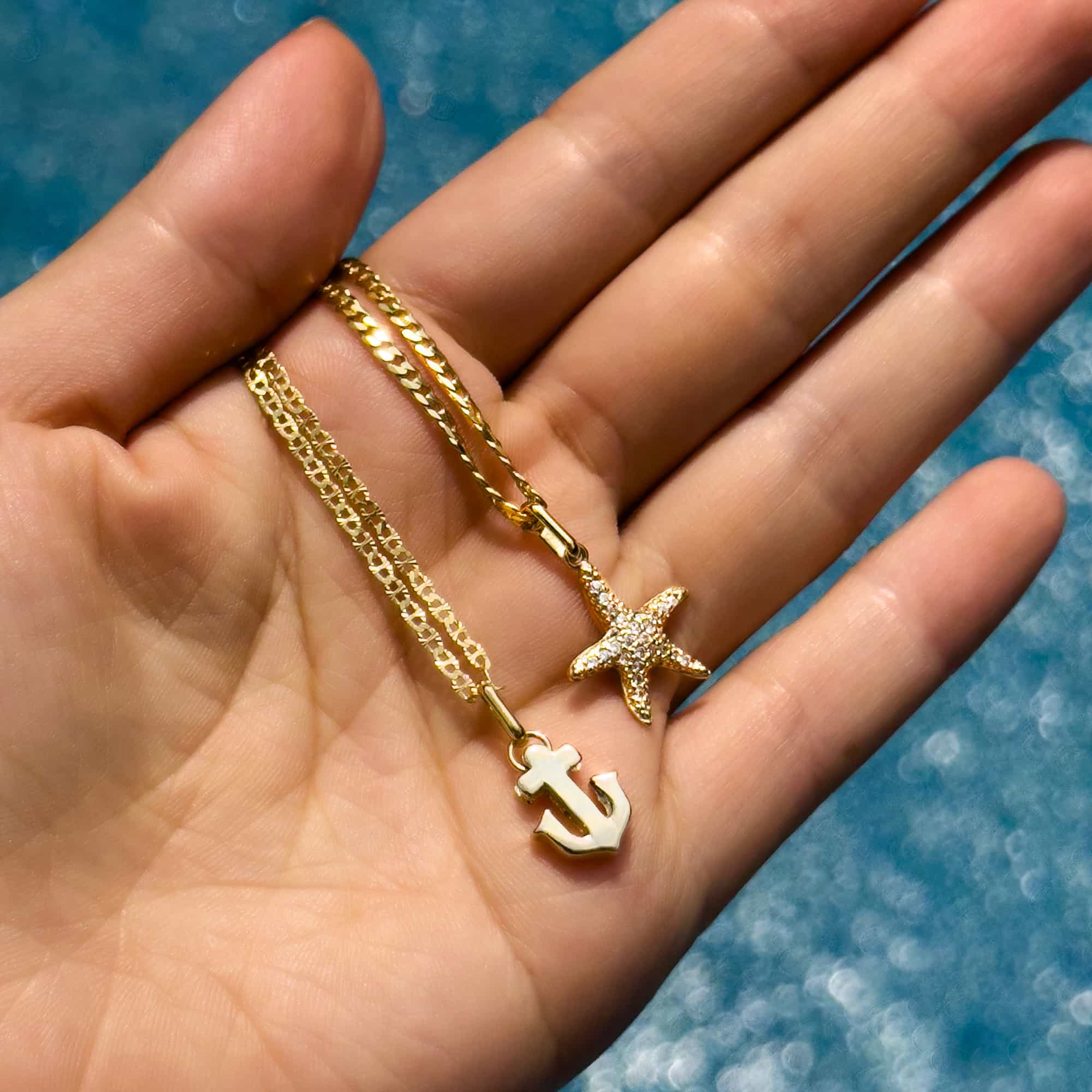 Gold anchor charm and a pavé starfish charm on chains, held in an open palm