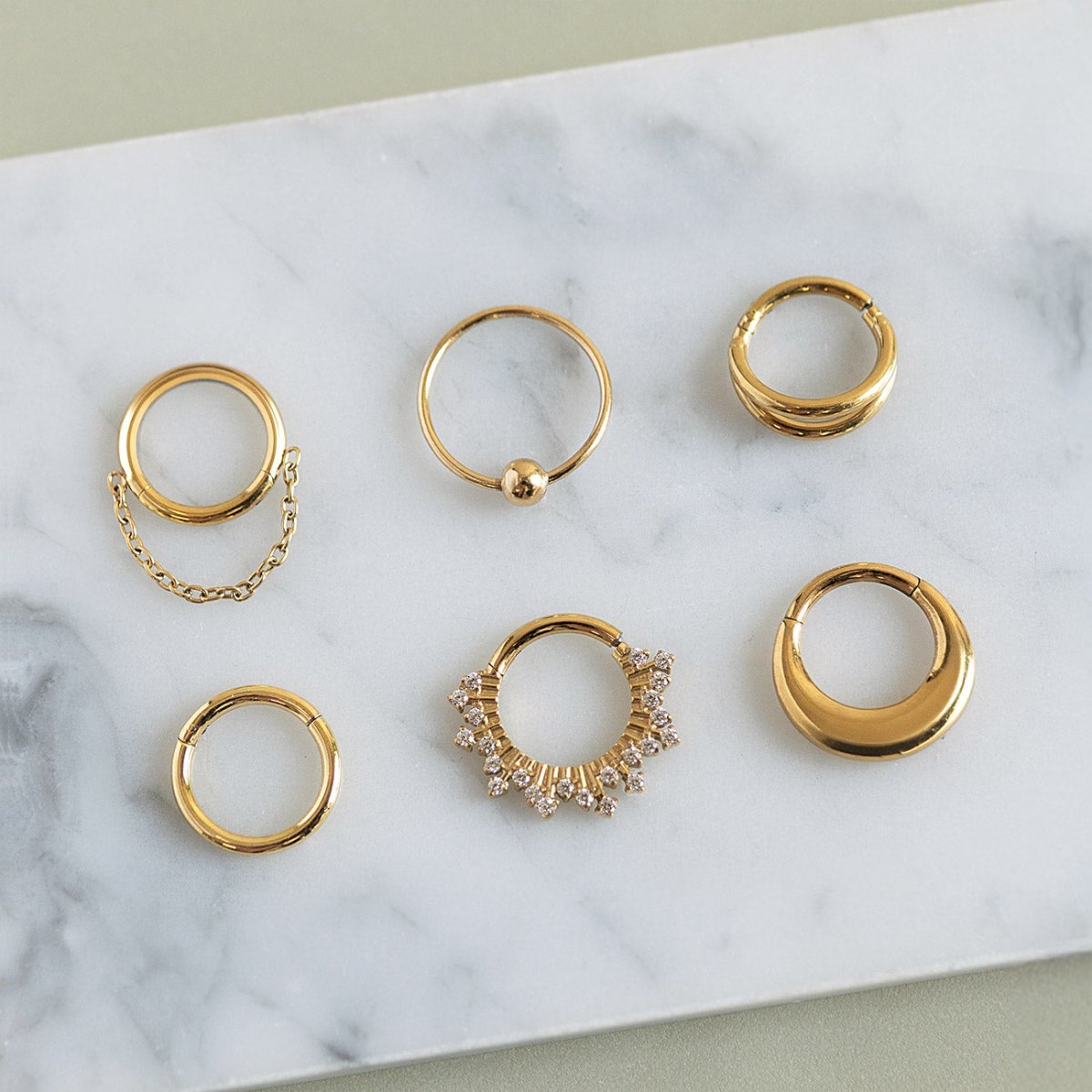 Assortment of gold clicker hoops and seamless rings, including a pavé and a chain-draped style, on white marble