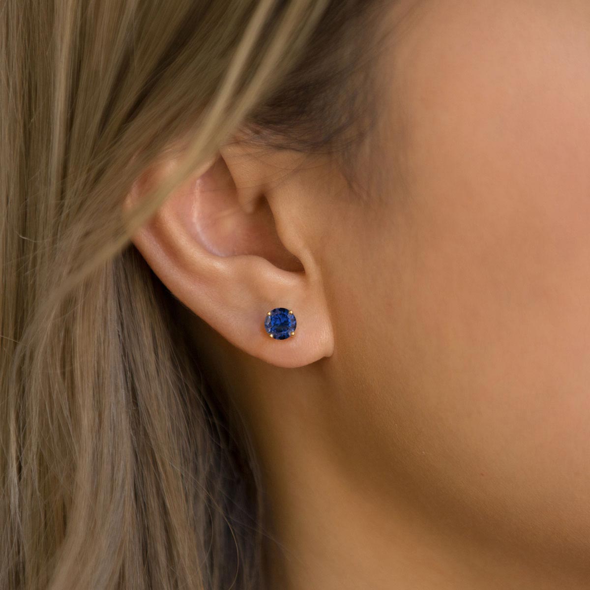 Birthstone stud earrings in many colors set in white gold prongs, arranged on white marble steps