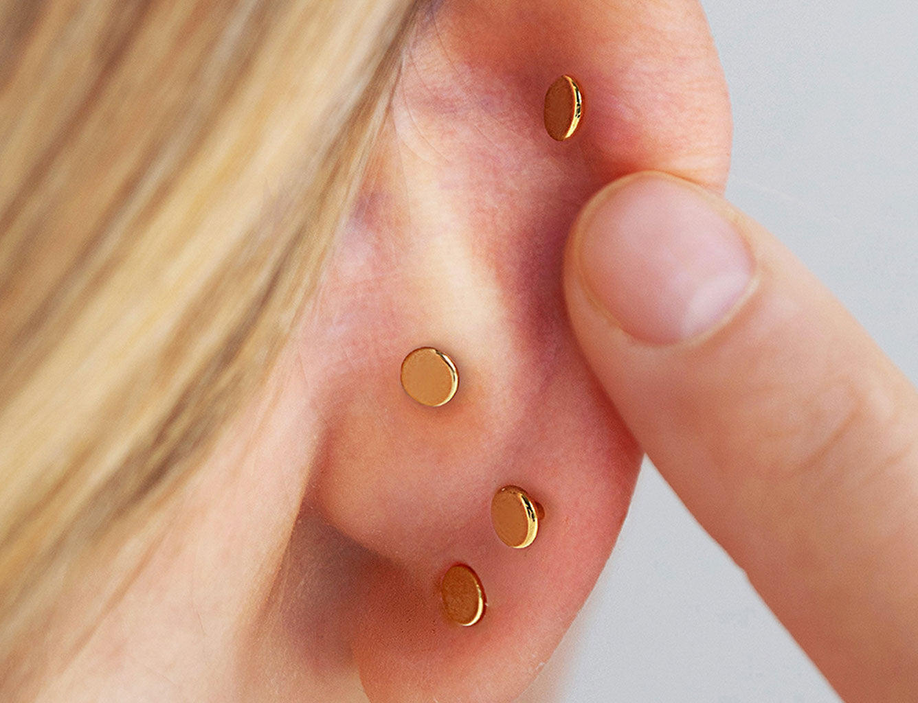 Close-up of an ear with four small round gold flat back studs worn in helix, conch and lobe piercings