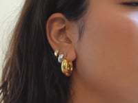 Close-up of woman's ear wearing gold chunky hoop, gold vermeil bold baguette huggie hoop, and sterling silver boyfriend huggie