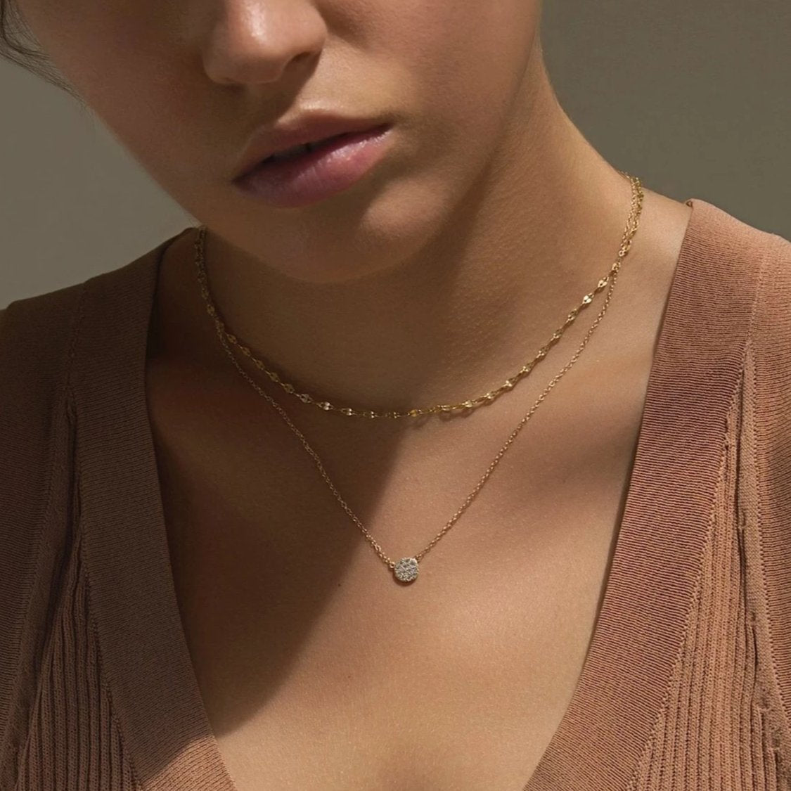 Gold vermeil layered necklace duo with a round pavé disc pendant set with clear stones, on a model's neckline
