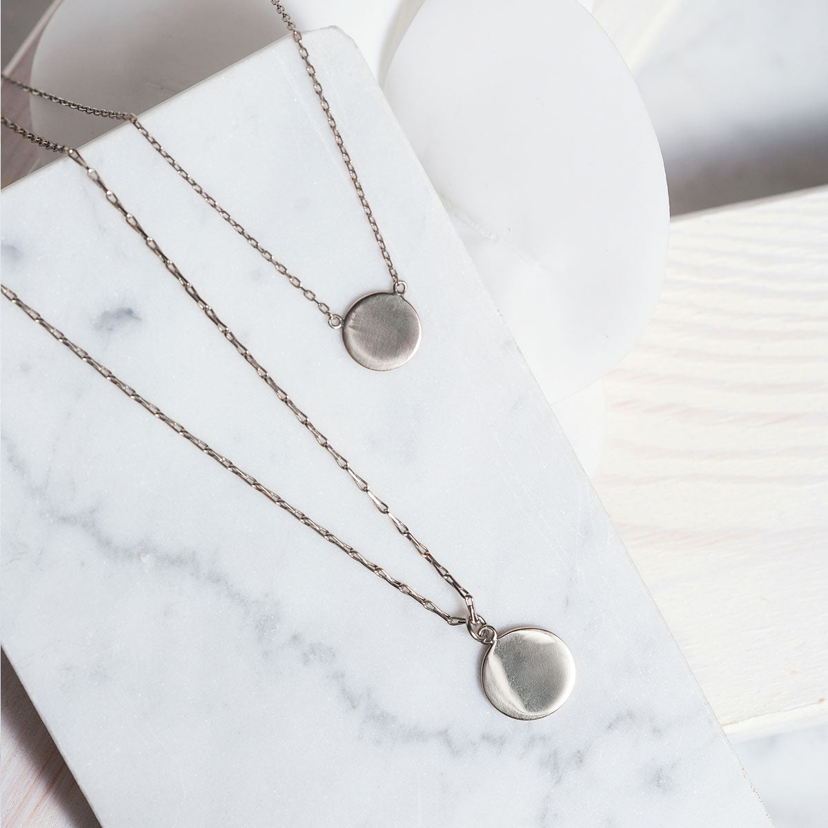 Sterling silver layered disc pendant necklaces laid on white marble