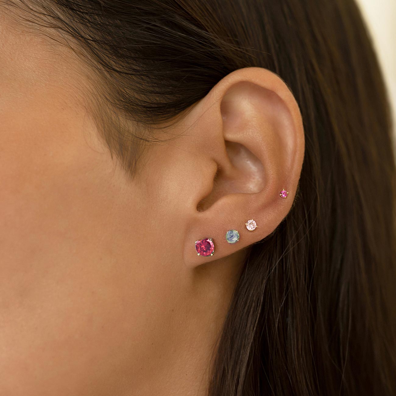 Sterling silver ruby stud with a round red stone, shown on a model's lobe in an ear stack