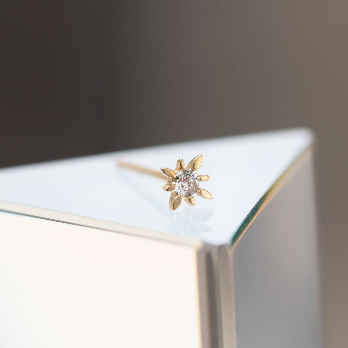 14K gold diamond starburst stud, close-up detail on a mirrored surface