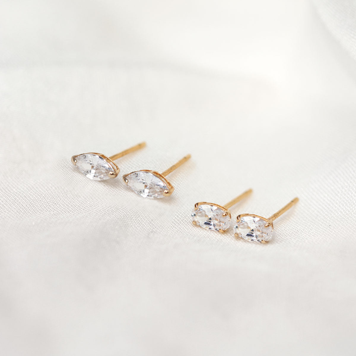 14K gold studs with clear marquise and oval white zirconia stones, on cream fabric