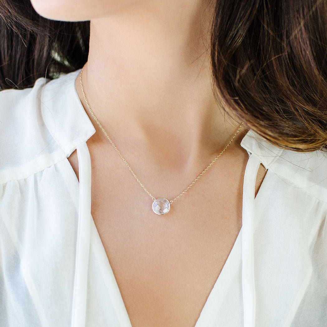 Gold vermeil necklace with a round faceted clear stone pendant, shown on a model's neckline