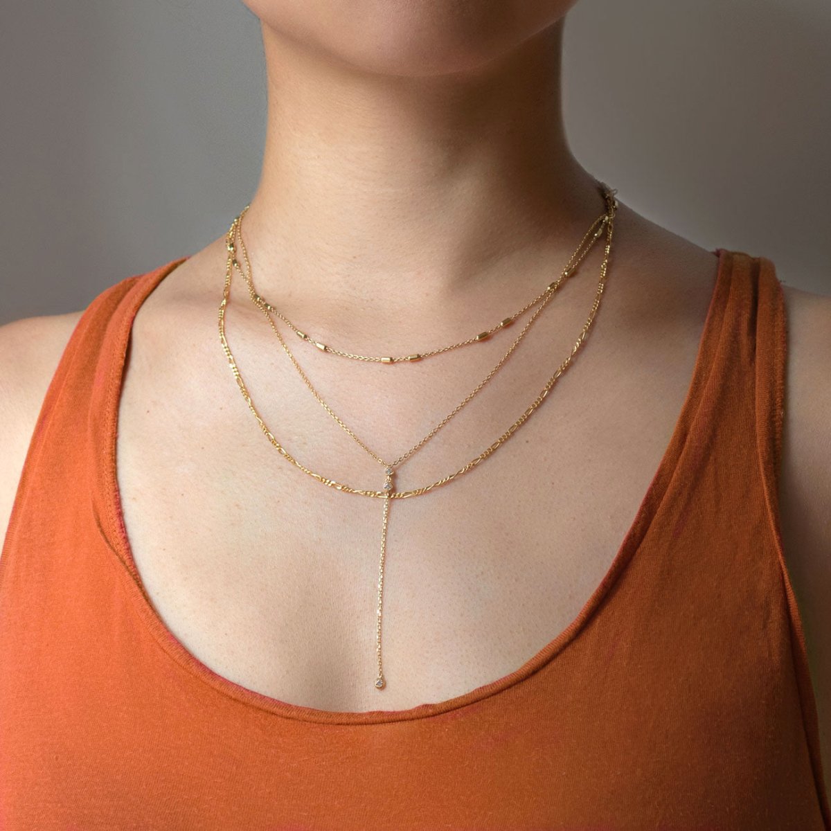 Gold vermeil layered necklace with a delicate lariat drop, shown on a model in an orange top
