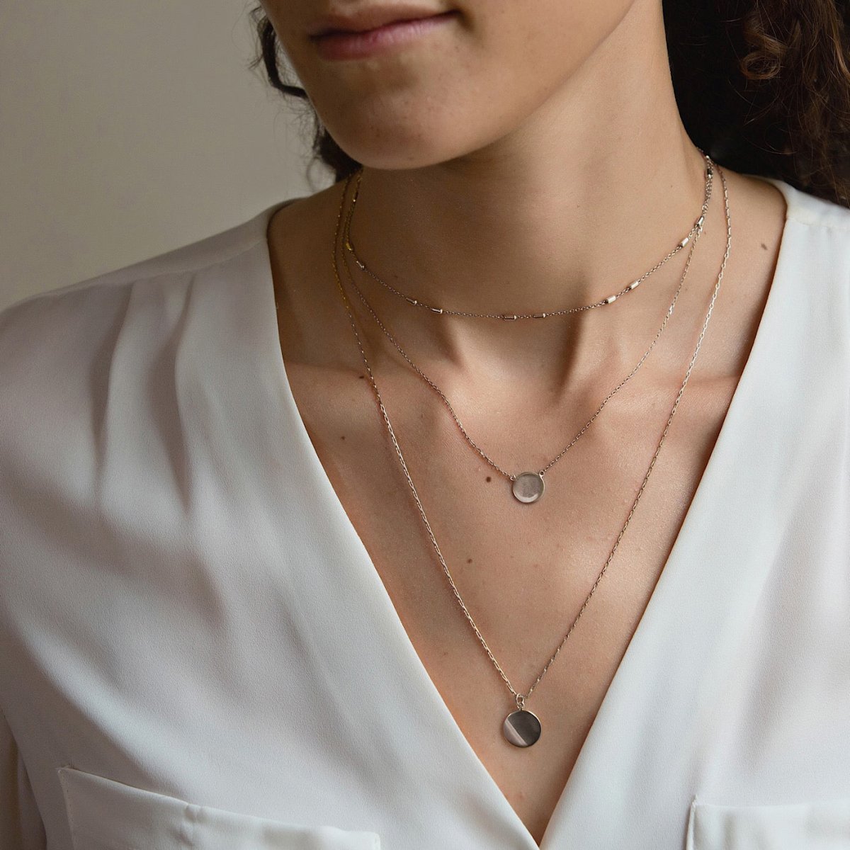 Sterling silver layered necklace with round disc pendants, shown on a model in a white blouse