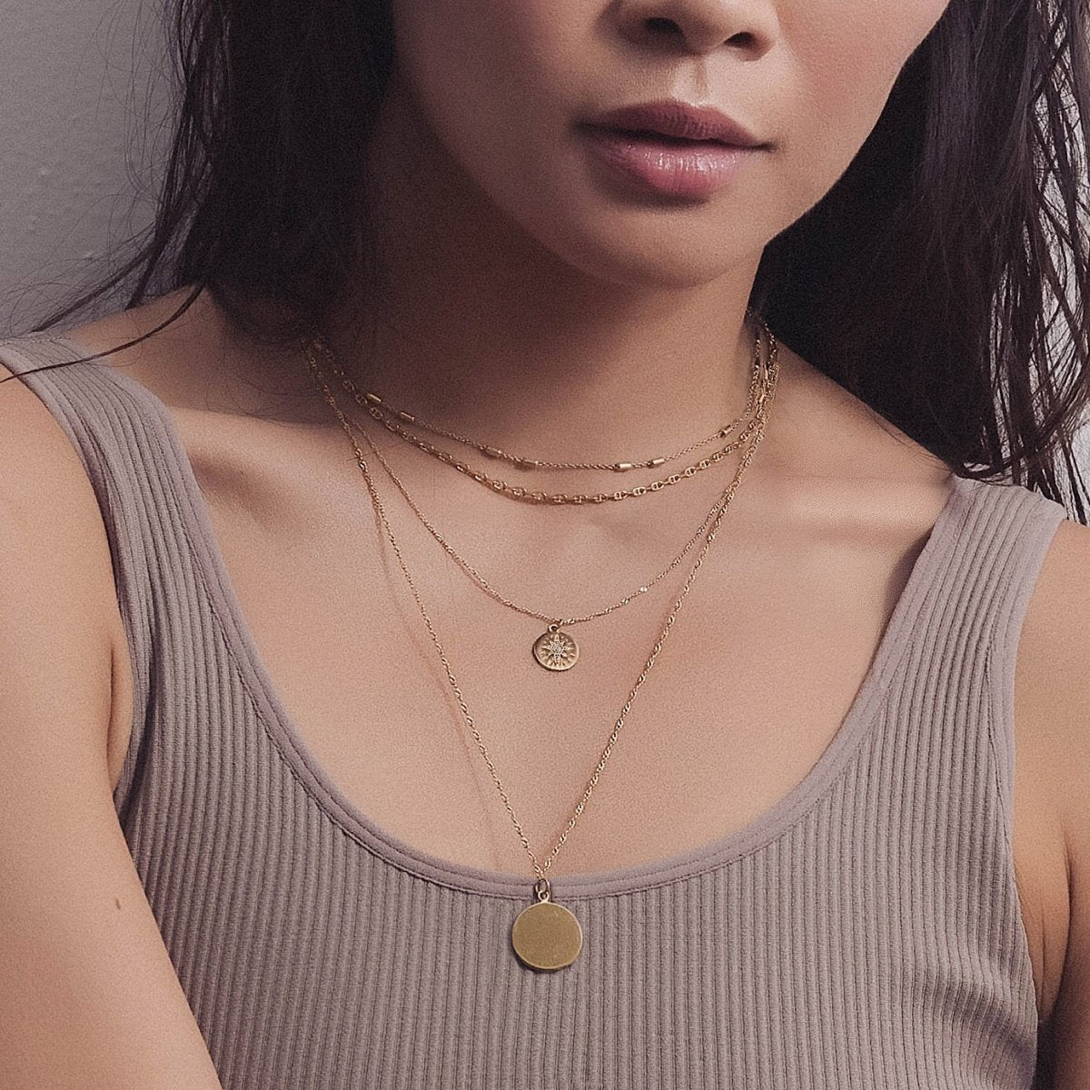 Gold vermeil star disc necklace with a starburst pendant, layered and shown on a model's neckline