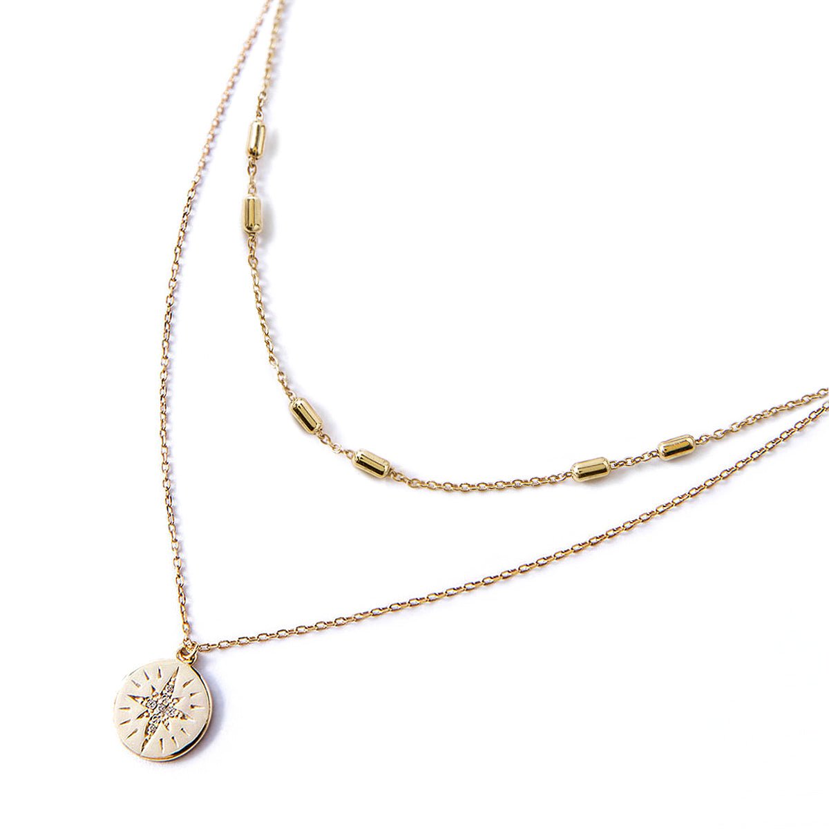 Gold vermeil layered necklace duo with a starburst disc pendant set with a clear stone, on a white background
