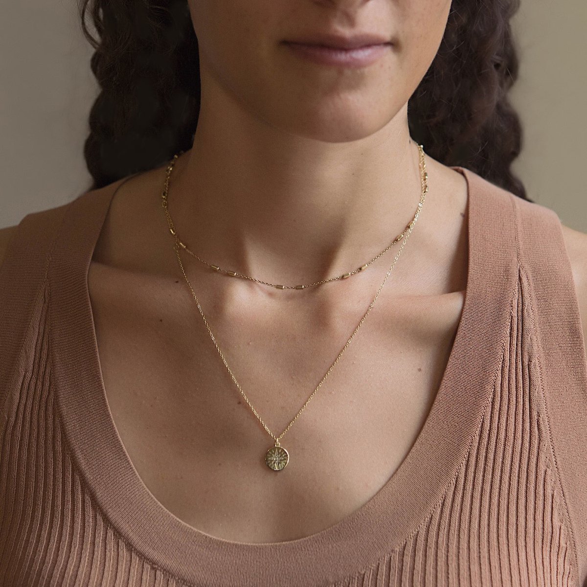 Gold vermeil layered necklace duo with a starburst disc pendant, shown on a model's neckline
