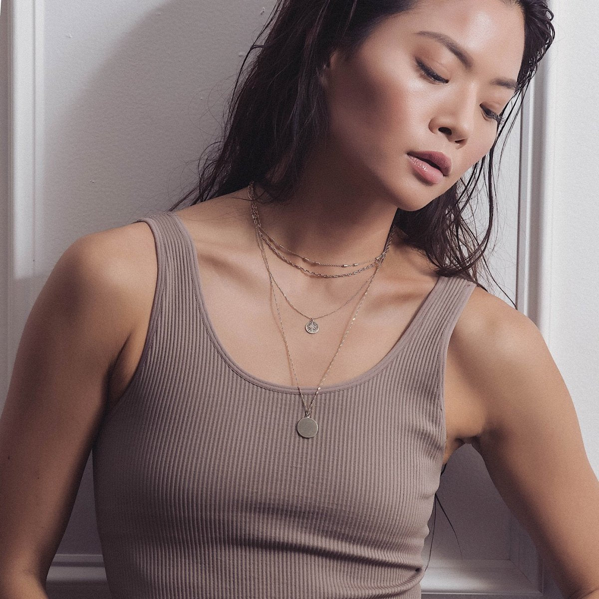Sterling silver layered chains with a round disc pendant shown on a model's neckline